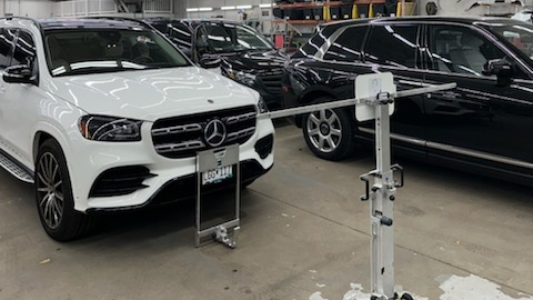 A white Mercedes SUV sits inside an automotive workshop with calibration equipment positioned in front of its grille.